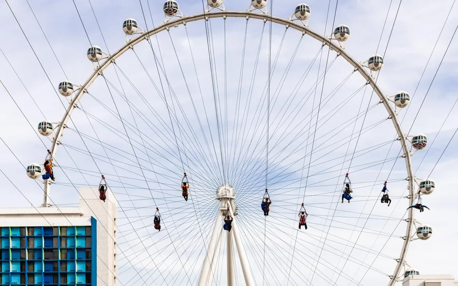 A zipline rider in flight above the promenade with the High Roller behind