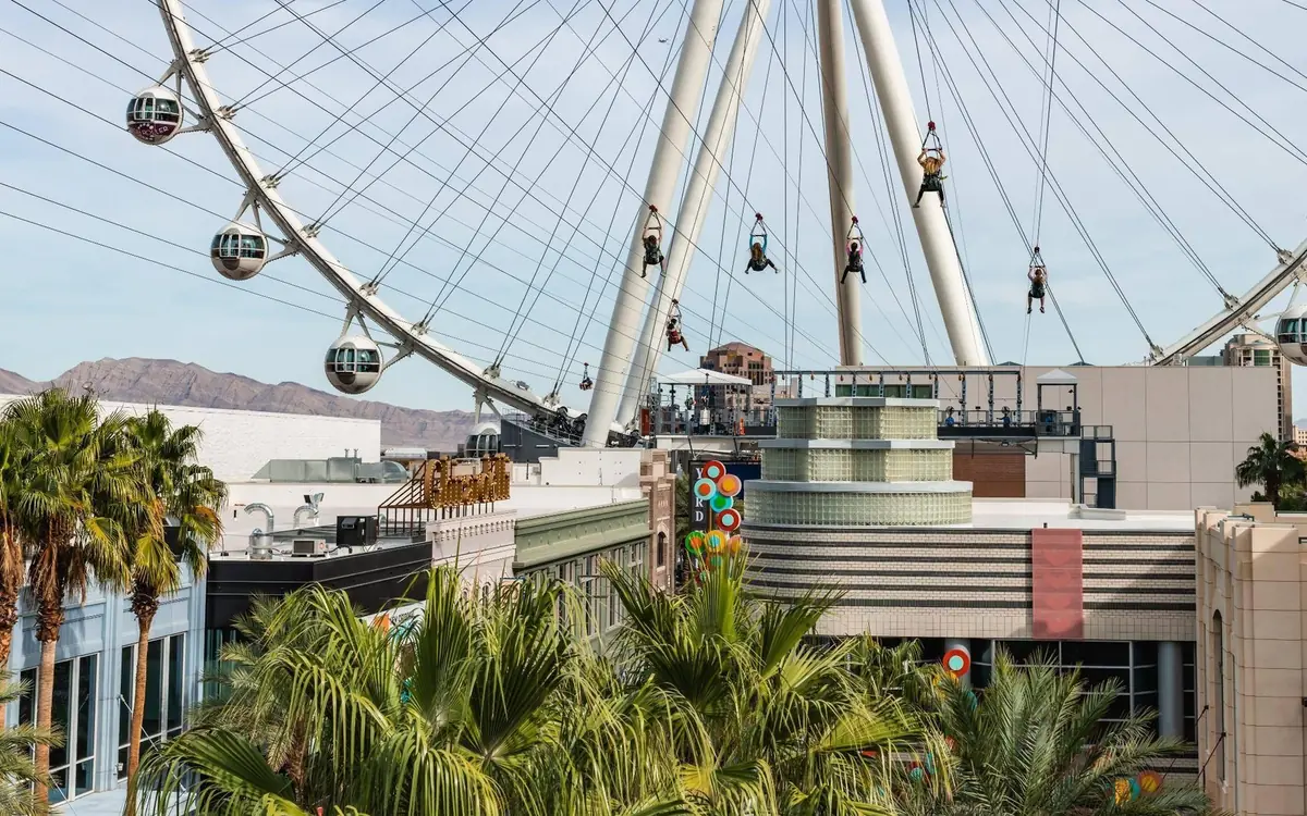 Zipline riders in flight with the High Roller wheel behind them